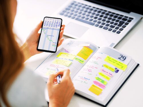 Woman planning with smartphone, planner, laptop. Productivity, organization, time management, modern workspace.