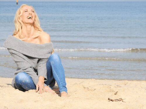 Dr. Madisen Harper in a gray sweater on a serene beach, embracing fun and flow in nature's tranquility and warmth.