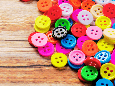 Colorful buttons scattered on wooden surface, showcasing vibrant hues and a black contrast button.