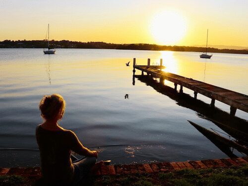 Serene sunset scene with Dr. Madisen Harper on a rustic dock with vibrant reflections and distant silhouetted boats.